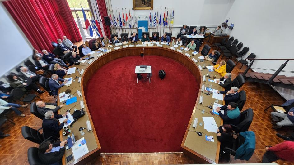 Mesa grande con muchas personas sentadas y las banderas patrias al fondo